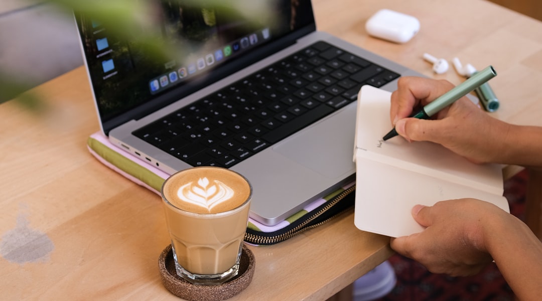 Person writing in notebook beside a laptop and coffee